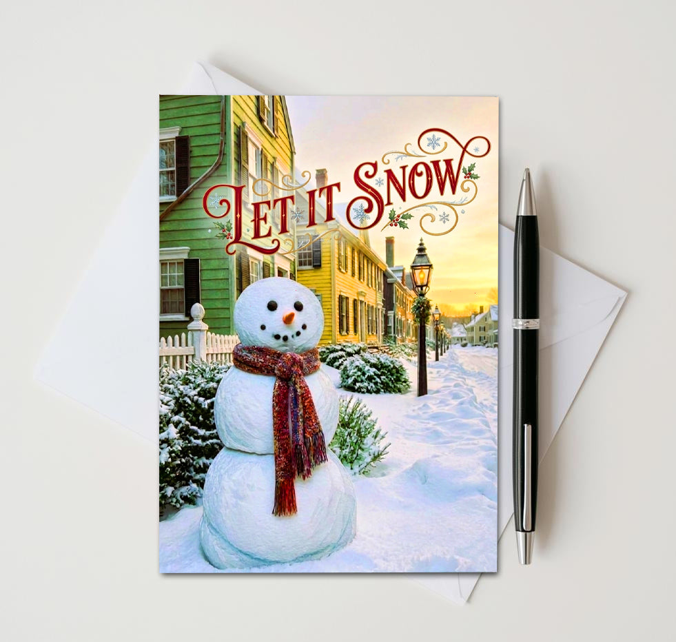 Let It Snow card with red-scarf snowman on a snowy street lined with colorful houses
