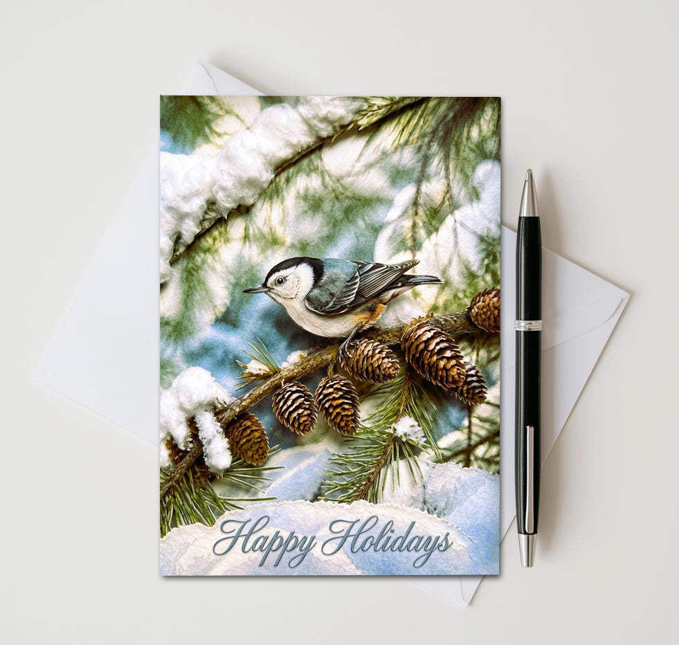 Happy Holidays card with nuthatch on snowy pine branches and pinecones, beside an envelope and pen
