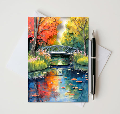 Greeting card with a colorful autumn scene of a bridge over a pond, pen and envelope on the side.