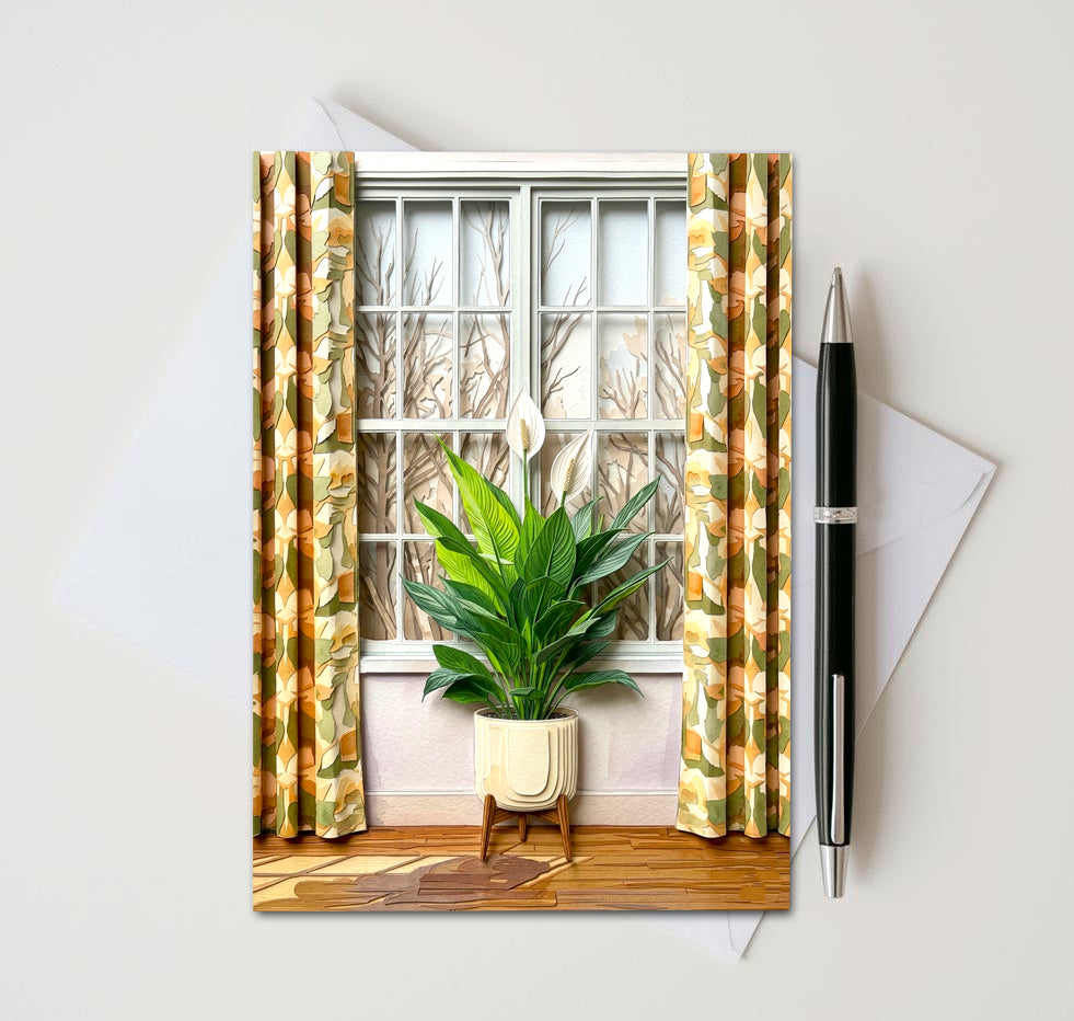 Note card with a peace lily plant in front of a window as subject. Card sitting on white surface with a pen next to card and envelope