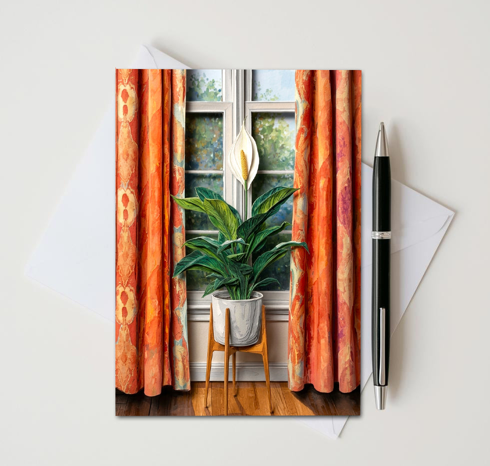 Note card with a peace lily plant in front of a window as subject. Card sitting on white surface with a pen next to card and envelope