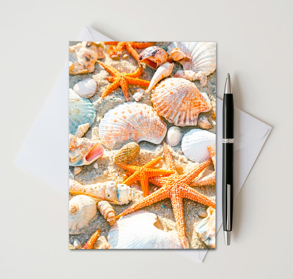 Greeting card with starfish and shells design on a white surface with a pen and envelope.