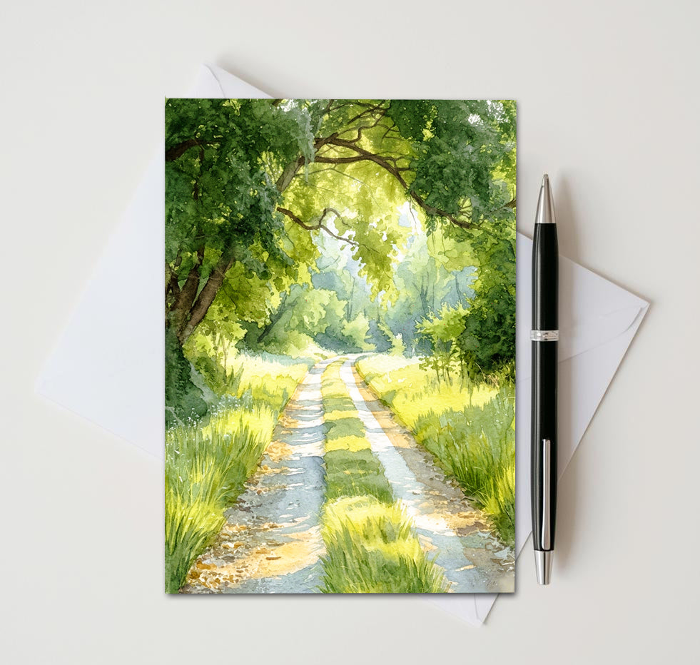 Greeting card with a scenic illustration of a sunlit path through trees, accompanied by a pen and envelope on a white background.