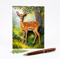 Card with a deer illustration in a forest setting and a pen on a white background