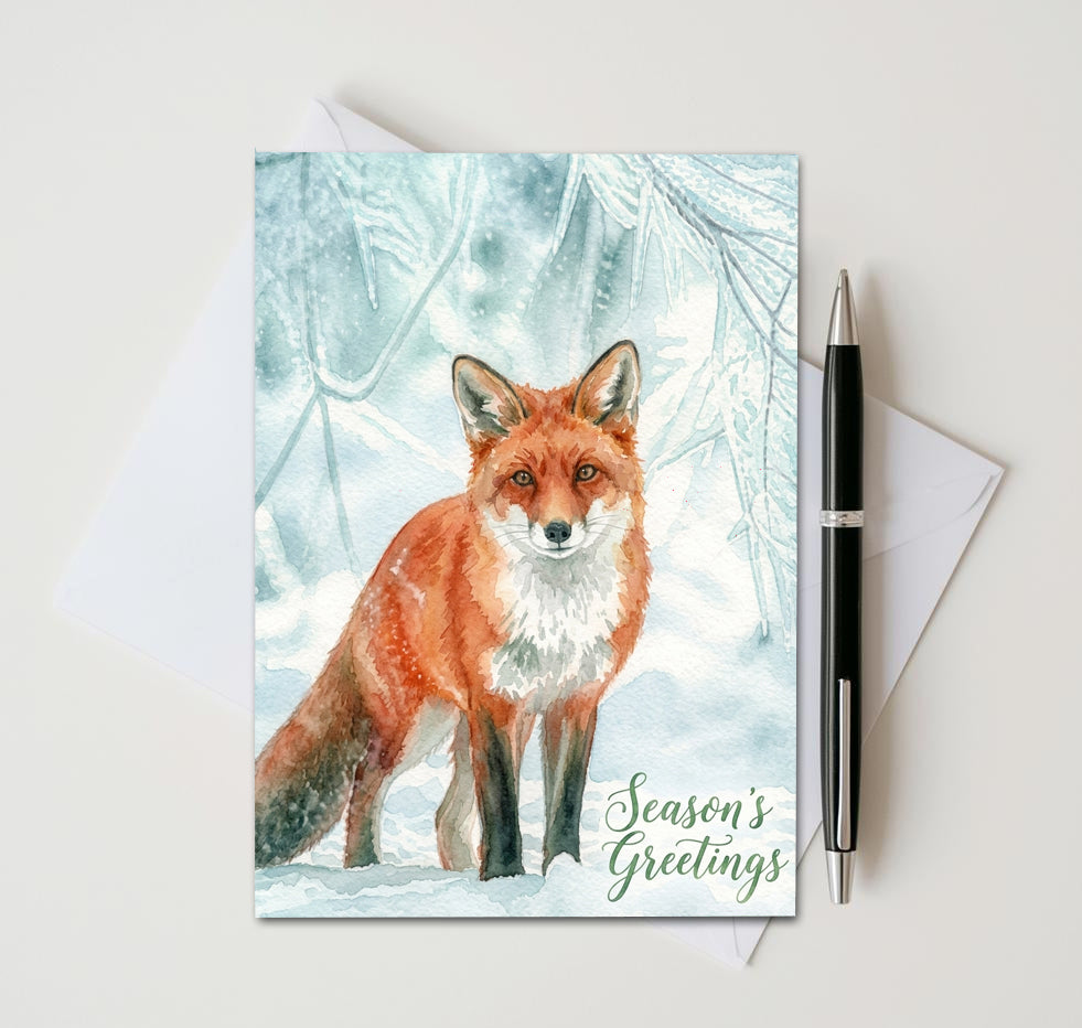 Season’s Greetings card with red fox beneath frosty branches, beside an envelope and pen
